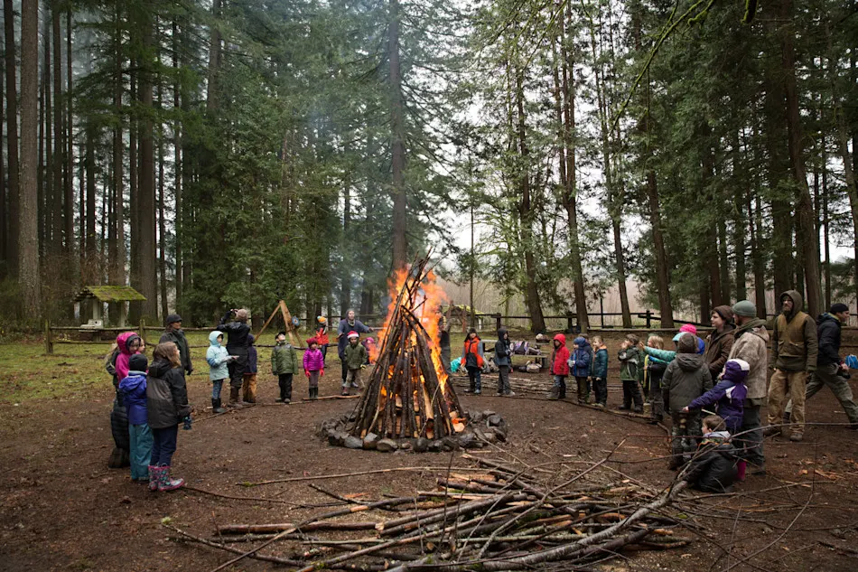 A circle of bundled-up kids and Guides gathered around a tall winter bonfire in the forest