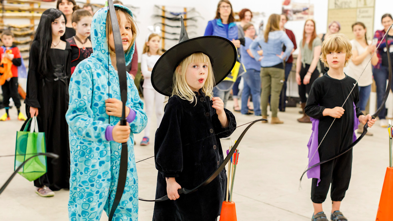 Students in Halloween costumes shooting bows at Track-or-Treat while families watch