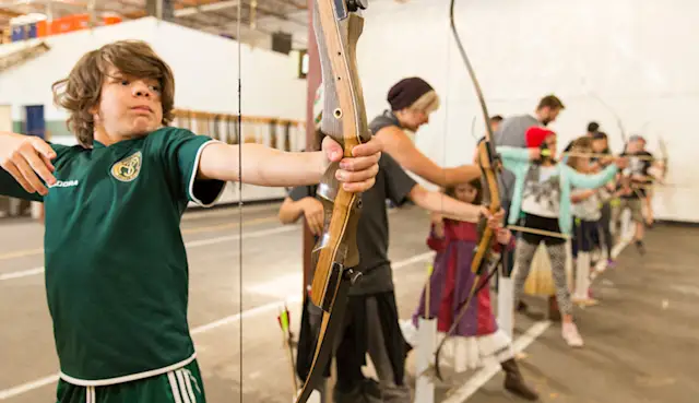 Kid drawing a bow on the line at the Trackers SE indoor archery range