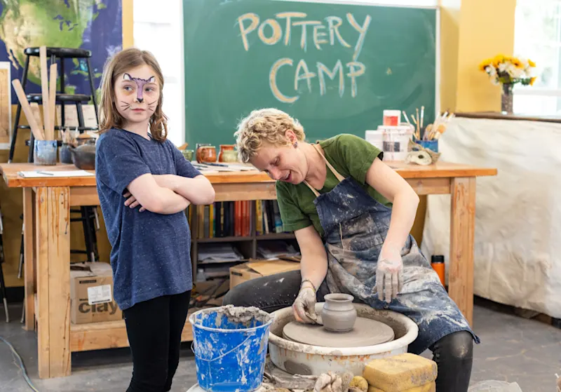 Kids with painted faces watching a pottery wheel demo