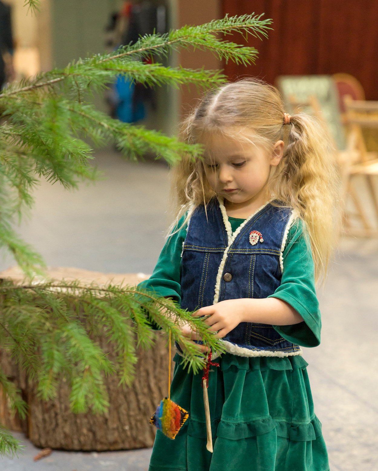 A young girl in green velvet hanging an ornament on an evergreen branch