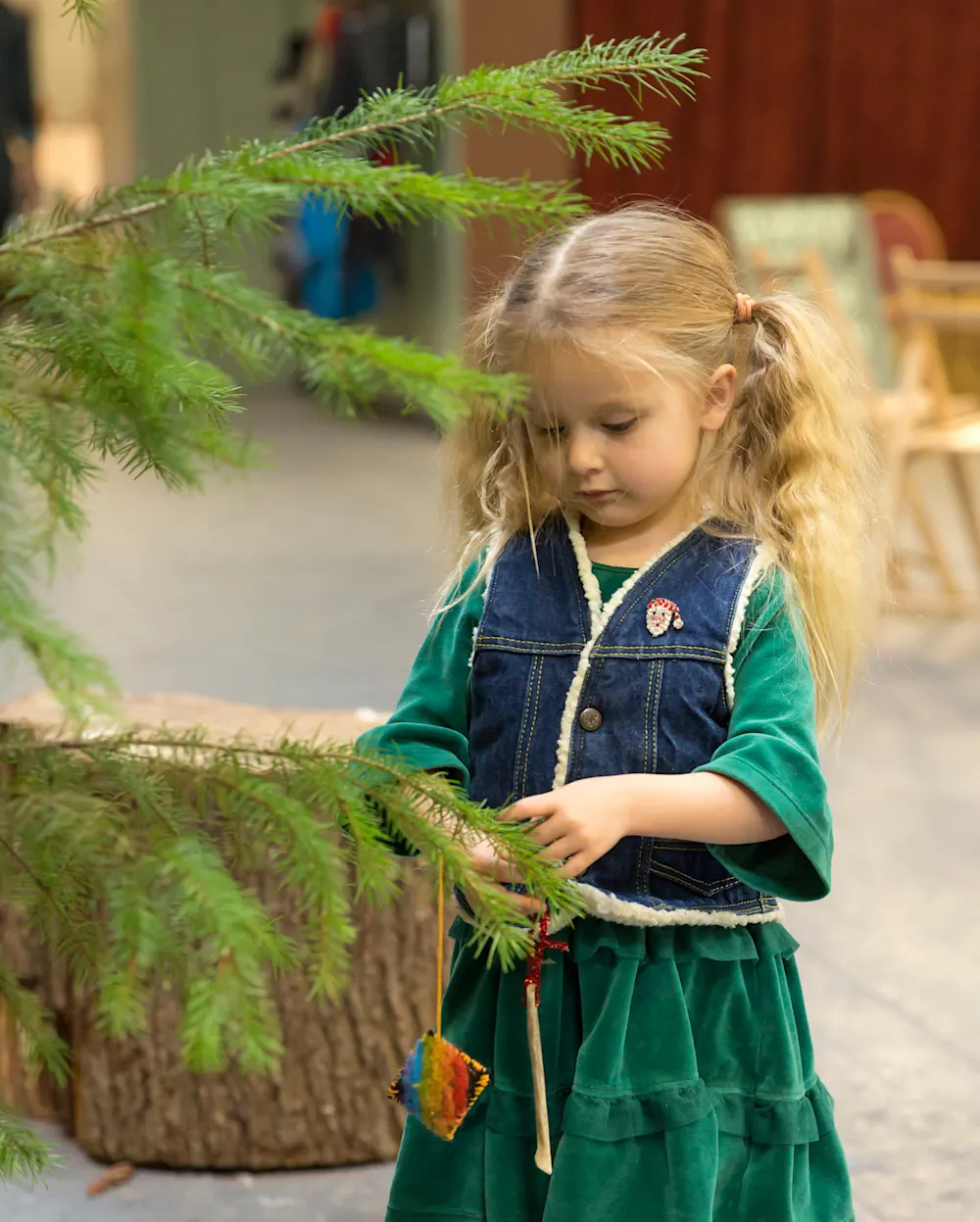 A young girl in green velvet hanging an ornament on an evergreen branch