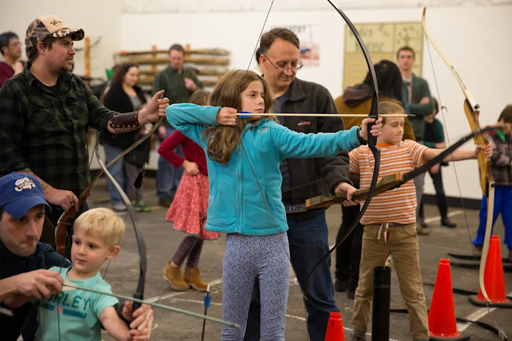 Families drawing bows on the indoor archery range at the Holiday Faire