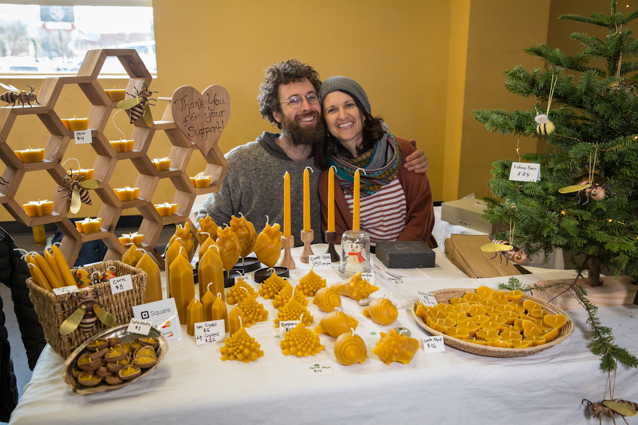 Two local makers behind a table of handmade beeswax candles