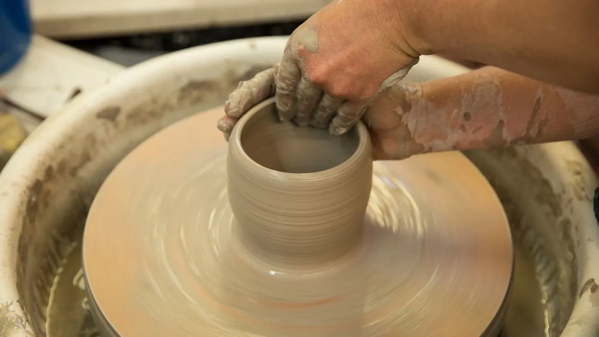 Hands shaping clay on the pottery wheel at Trackers