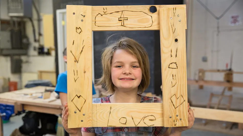 Kid showing a wood-burned picture frame in the Trackers woodworking shop