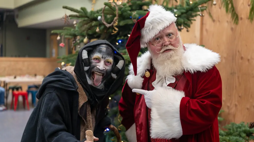 Santa Claus pointing at Krampus in front of the holiday tree
